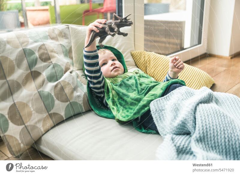 Boy in a costume lying on amattress playing with toy figure at home laying down lie lying down animal figurine animal figurines fancy dress fancy-dress costume