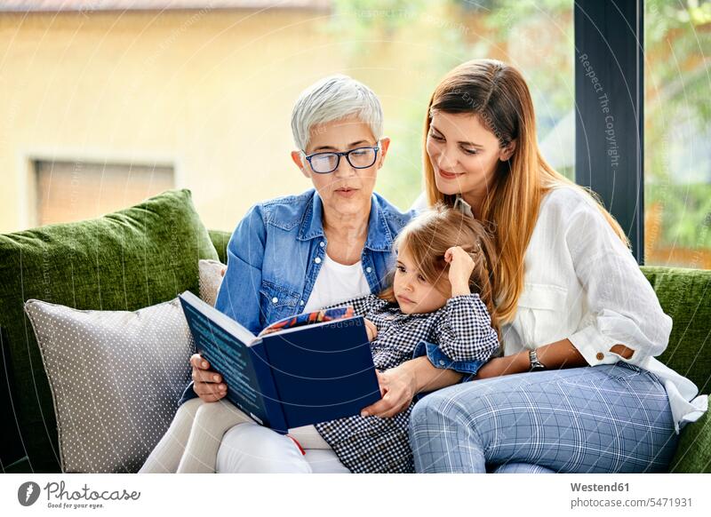 Mother, daughter and granddaughter sitting on couch, reading a book human human being human beings humans person persons caucasian appearance