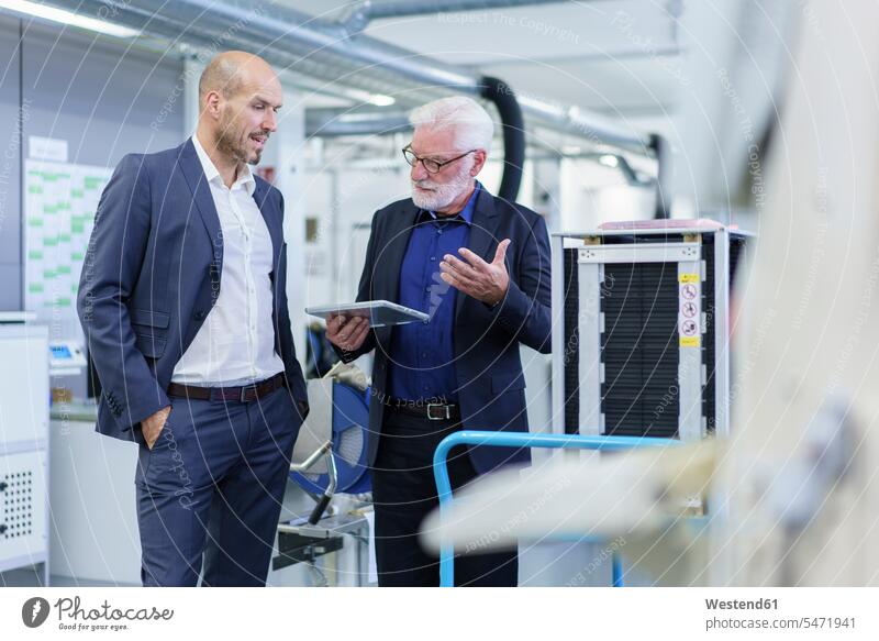 Senior male manager discussing over digital tablet with colleague while standing by machinery at factory color image colour image indoors indoor shot