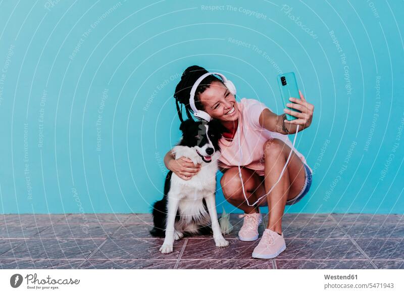 Happy woman taking selfie with Border Collie dog against turquoise wall color image colour image Spain outdoors location shots outdoor shot outdoor shots day