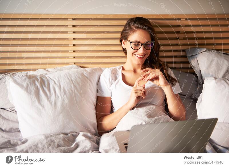 Portrait of smiling young woman lying on bed using laptop beds use laying down lie lying down females women portrait portraits smile Laptop Computers laptops