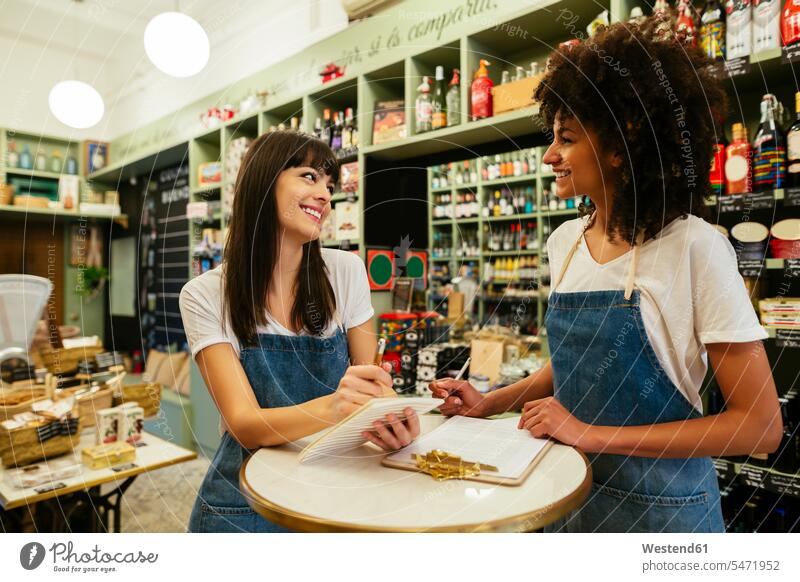 Two smiling women in a store taking notes smile woman females making a note note taking shop Adults grown-ups grownups adult people persons human being humans