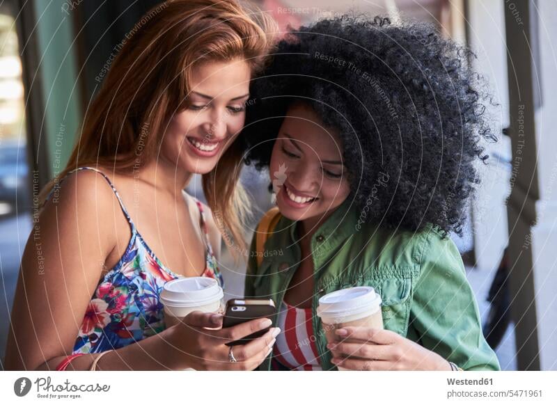 Girlfriends with coffee to go using smartphone telecommunication phones telephone telephones cell phone cell phones Cellphone mobile mobile phones mobiles hold