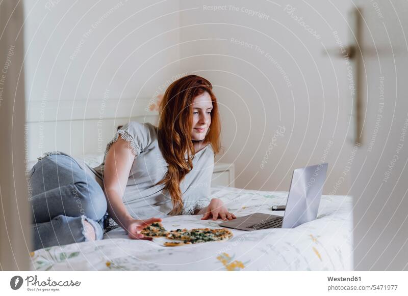 Beautiful woman lying while watching movie and enjoying pizza on bed at home color image colour image Spain leisure activity leisure activities free time