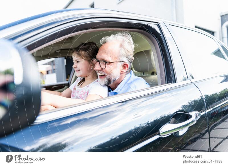 Little girl sitting on lap of grandfather, pretending to steer the car automobile Auto cars motorcars Automobiles summer summer time summery summertime