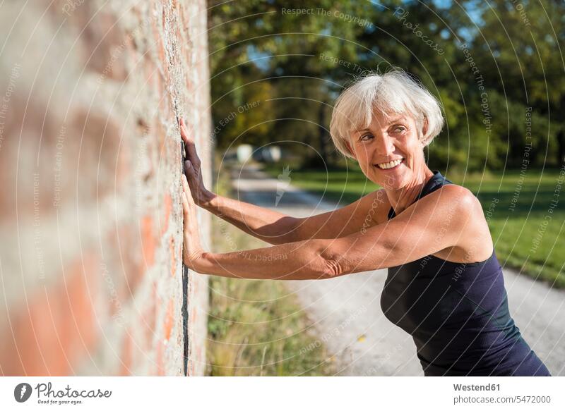 Smiling sportive senior woman leaning against a brick wall sporting sporty athletic females women smiling smile senior women elder women elder woman old sports