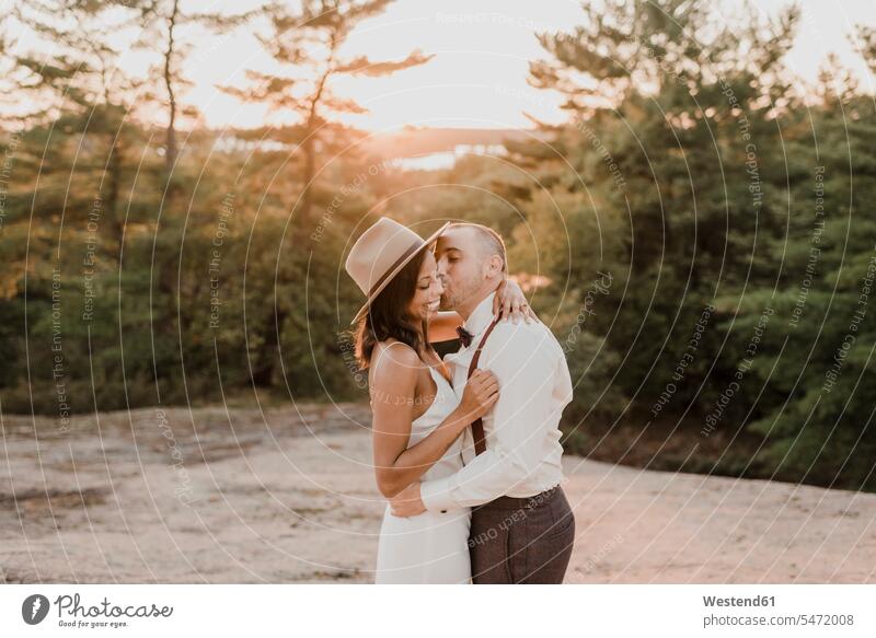 Couple kissing while standing on walkway in forest during sunset color image colour image outdoors location shots outdoor shot outdoor shots sunsets sundown