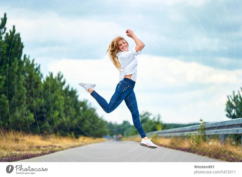 Cheerful woman jumping on rural road touristic tourists pants Trouser Denim Jeans smile summer time summertime summery relax relaxing relaxation delight