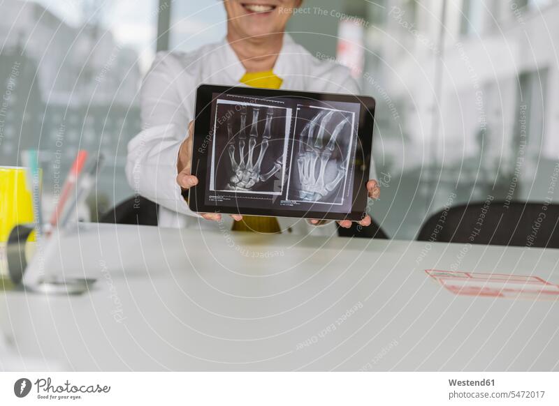 Doctor sitting at desk showing x-ray image of hand on digital tablet Occupation Work job jobs profession professional occupation images picture pictures