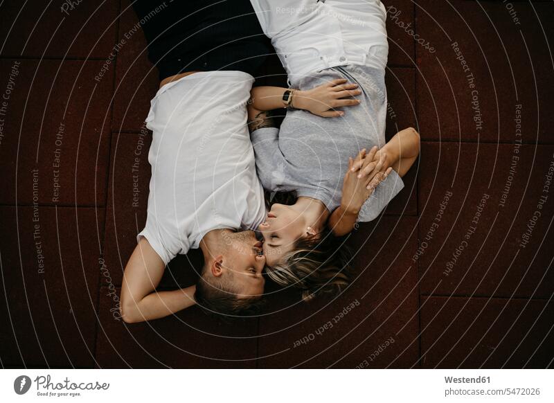 Young couple lying on the ground, from above relax relaxing cuddle snuggle snuggling embrace Embracement hug hugging in the evening delight enjoyment Pleasant