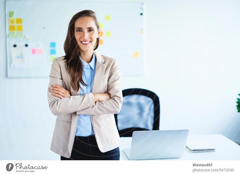 Cheerful young businesswoman looking at camera with crossed arms standing in office Occupation Work job jobs profession professional occupation business life