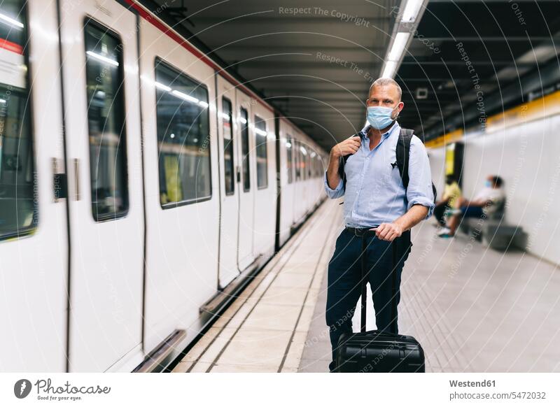 Businessman wearing face mask while standing with luggage at subway platform business people businesspeople Business Professional Business Professionals