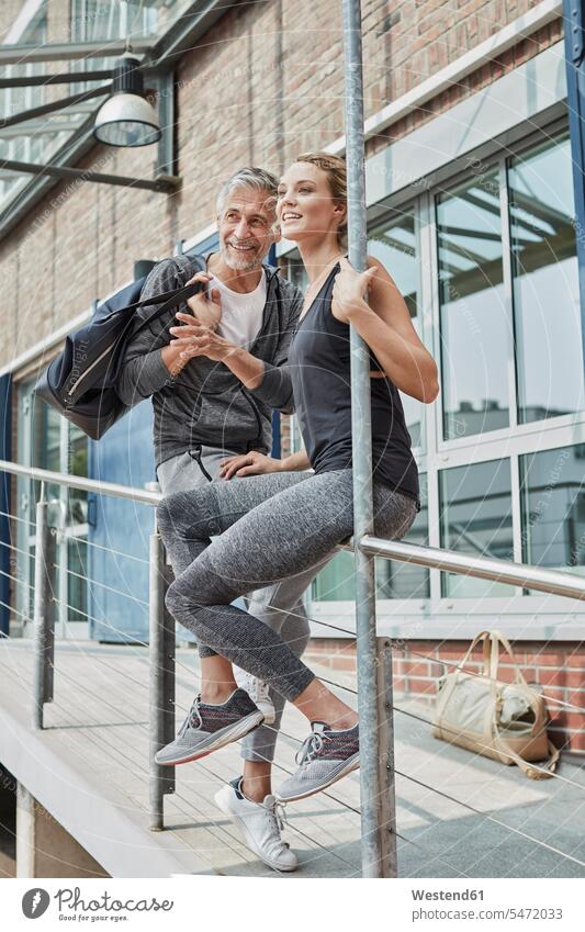 Portrait of mature man with sports bag and young woman in front of gym watching something gyms Health Club females women Gym Bag observing observe portrait
