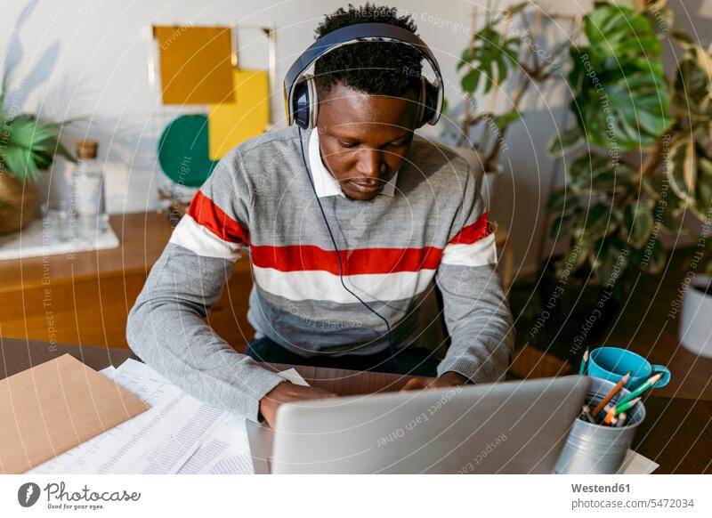 African businessman with headphones attending video call on laptop at home color image colour image indoors indoor shot indoor shots interior interior view