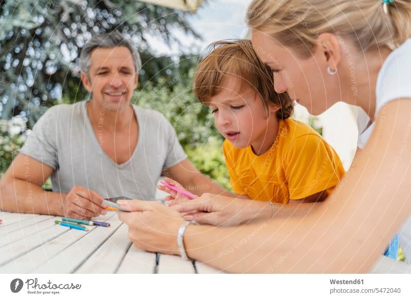 Father, mother and son doing homework together on terrace pupils schoolchild schoolchildren T- Shirt t-shirts tee-shirt Tables Seated sit summer time summertime