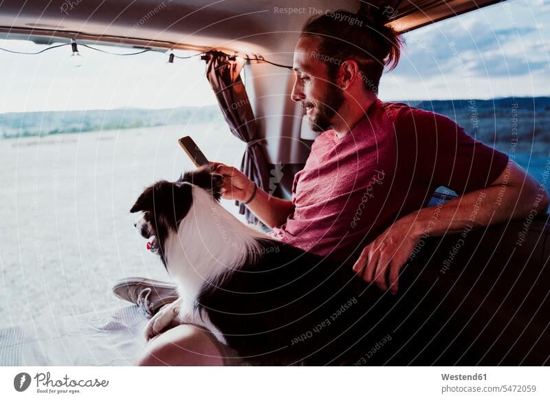 Smiling man using phone by dog in motor home color image colour image Spain leisure activity leisure activities free time leisure time dogs Canine domestic dog
