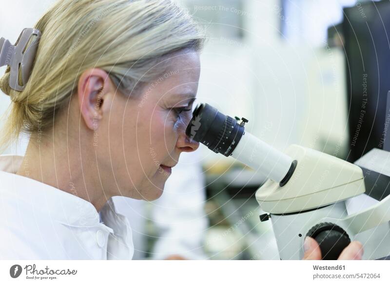 Blond female scientist looking through microscope at illuminated laboratory color image colour image indoors indoor shot indoor shots interior interior view