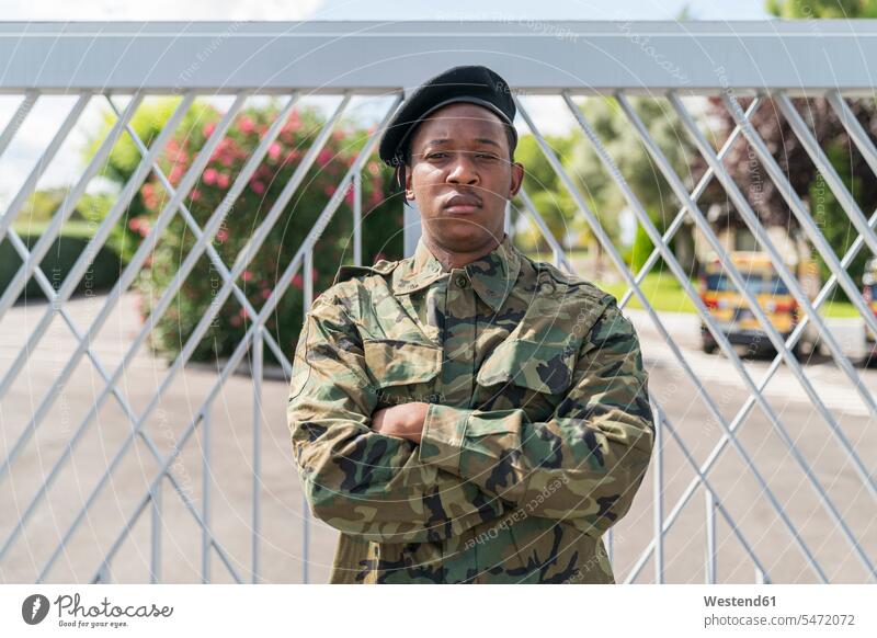 Confident army soldier standing with arms crossed against gate color image colour image outdoors location shots outdoor shot outdoor shots day daylight shot