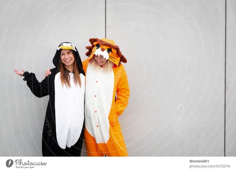 Two women in penguin and lion costume in front of concrete wall leo lions celebrate partying smile embrace Embracement hug hugging delight enjoyment Pleasant