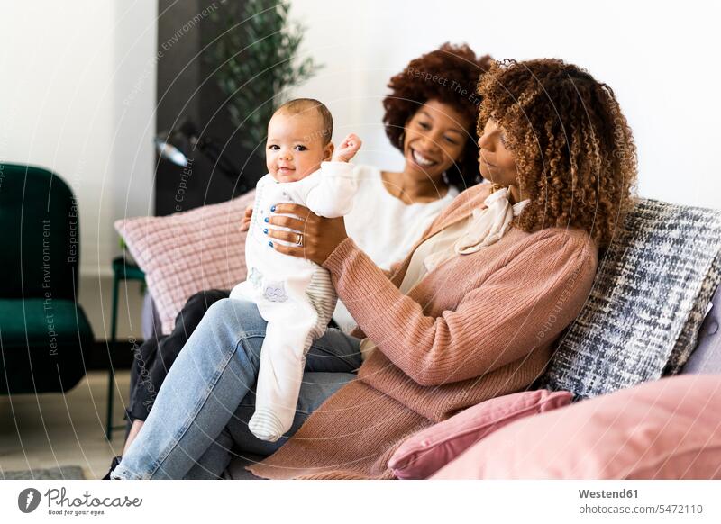 Smiling family sitting with baby girl on sofa at home color image colour image indoors indoor shot indoor shots interior interior view Interiors 2-5 months