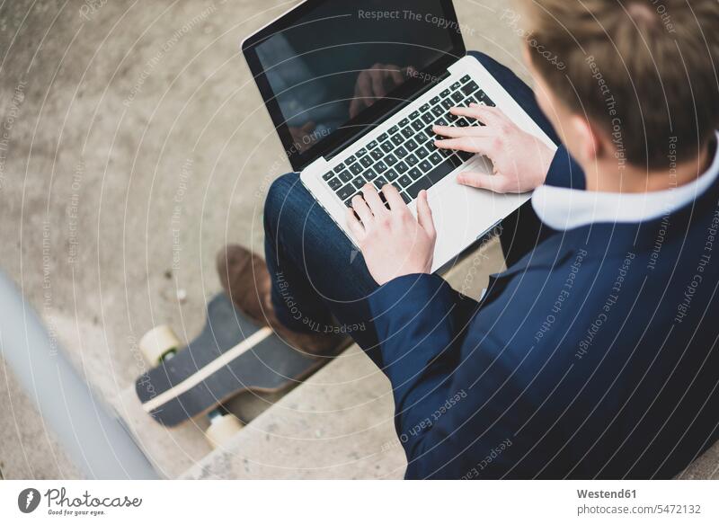 Young businessman with skateboard sitting outdoors on stairs using laptop men males Businessman Business man Businessmen Business men Laptop Computers laptops