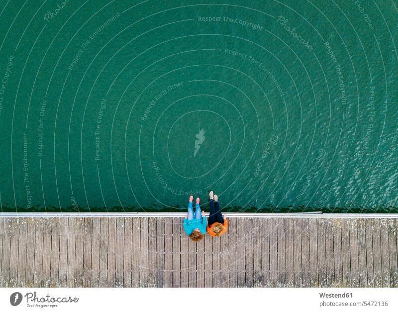 Two friends sitting side by side on jetty, Valdemurio Reservoir, Asturias, Spain relax relaxing Seated speak speaking talk enjoy enjoyment indulgence indulging