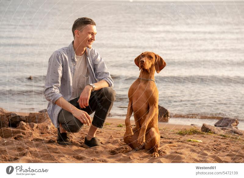 Young man with his dog at the beach during training animals creature creatures pet Canine dogs smile in the evening happy Contented Emotion pleased being proud