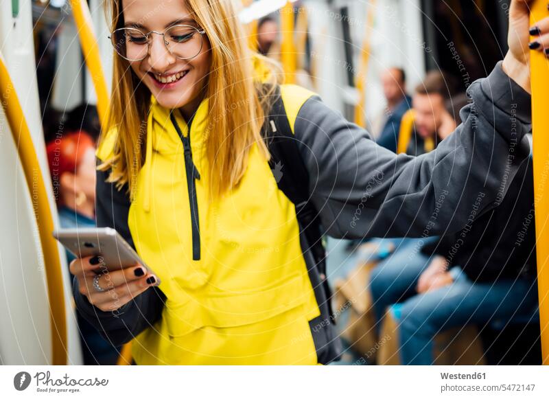 Smiling young woman standing in underground train using her smartphone touristic tourists back-pack back-packs backpacks rucksack rucksacks transport railroad