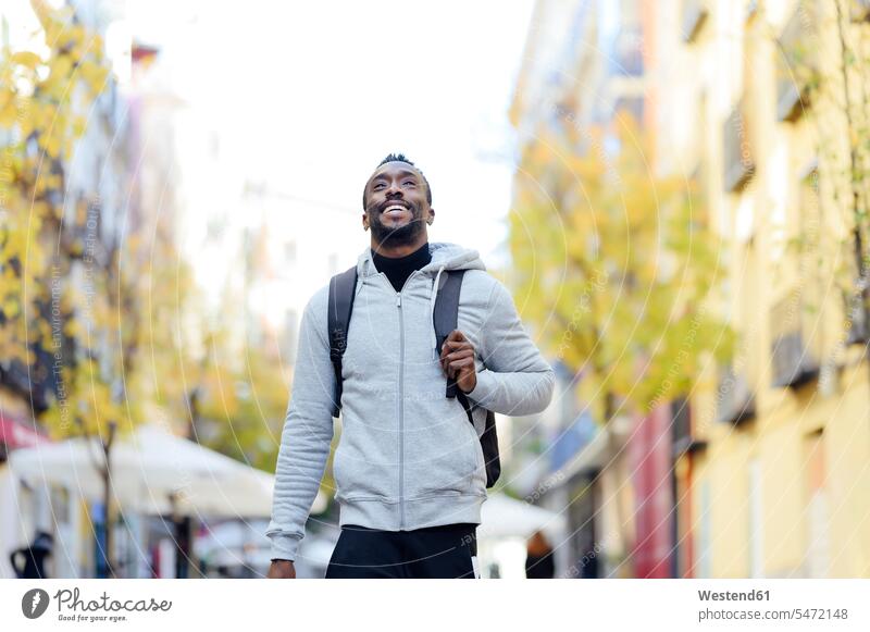 Young man with backpack smiling while walking in city color image colour image outdoors location shots outdoor shot outdoor shots day daylight shot