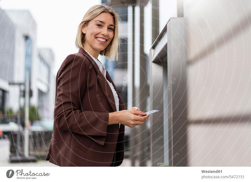 Portrait of smiling young businesswoman withdrawing money at an ATM in the city business life business world business person businesspeople business woman