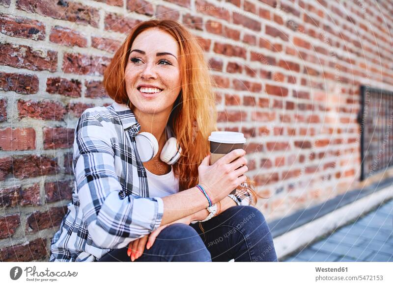 Young woman sitting against brick wall holding cup of coffee and looking away human human being human beings humans person persons caucasian appearance