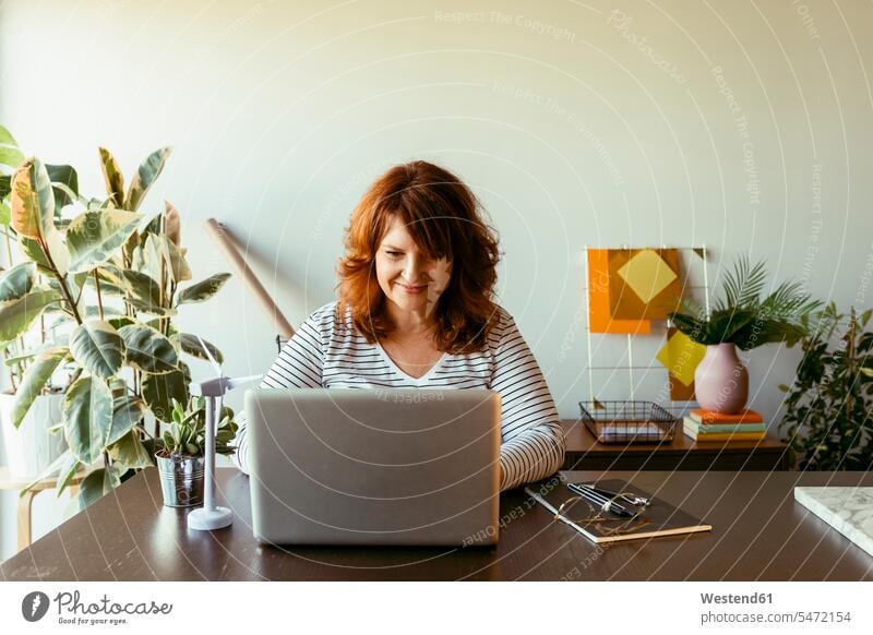 Mature woman working on laptop while sitting by table at home color image colour image indoors indoor shot indoor shots interior interior view Interiors day