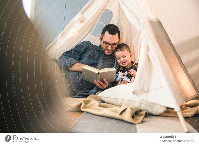 Father and son reading a book together in tent at home books tents father pa fathers daddy dads papa sons manchild manchildren parents family families people