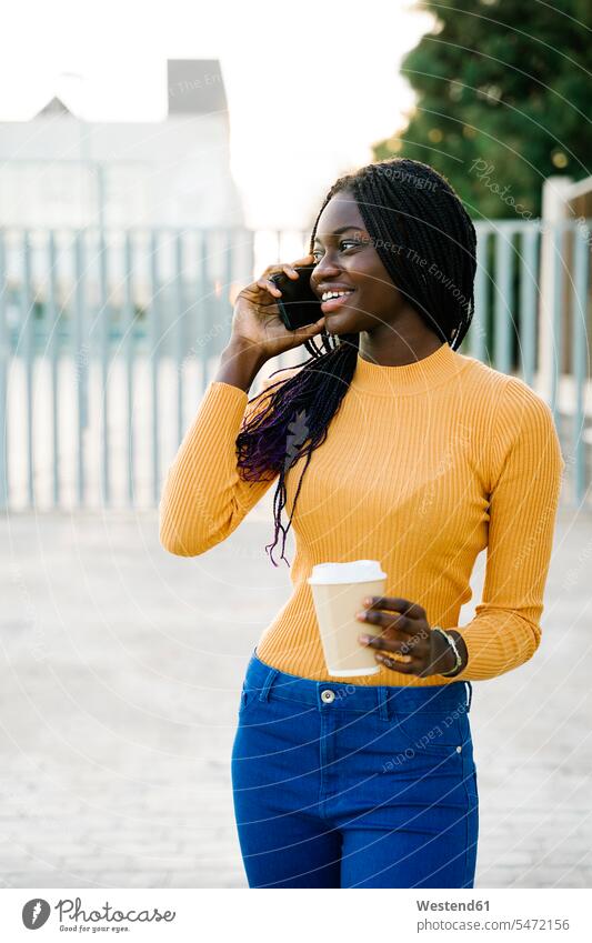 Happy teenage girl with coffee cup looking away while talking on smart phone at street color image colour image outdoors location shots outdoor shot