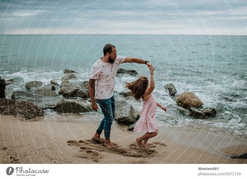 Daughter dancing with father at beach color image colour image outdoors location shots outdoor shot outdoor shots dusk evening twilight in the evening