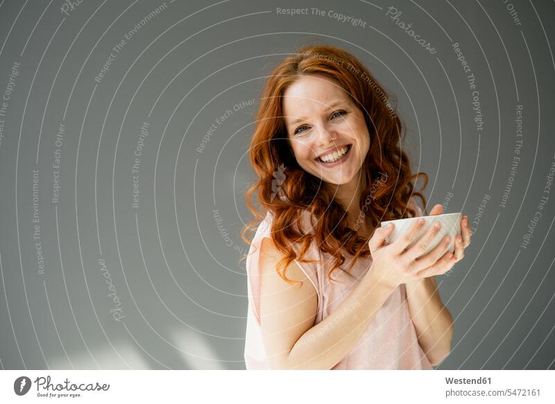 Portrait of happy redheaded woman with cereal bowl against grey background relax relaxing relaxation delight enjoyment Pleasant pleasure Cheerfulness