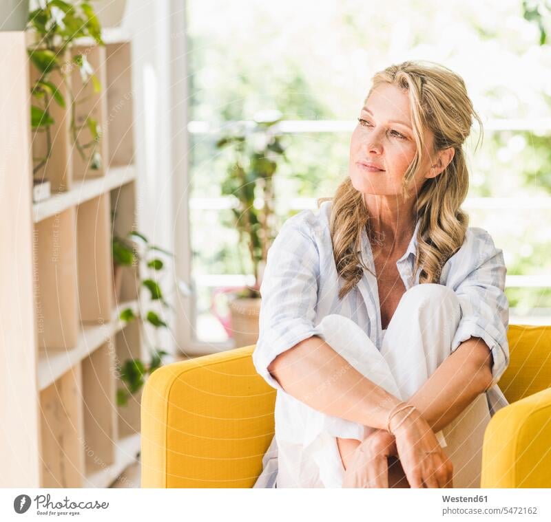 Portrait of pensive mature woman at home rack racks Shelve shelves relax relaxing Seated sit contemplative pensively Reflective thoughtful colour colours