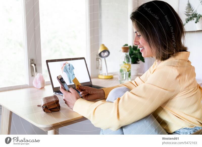 Happy young woman using credit card and smart phone for online shopping at home color image colour image Spain indoors indoor shot indoor shots interior