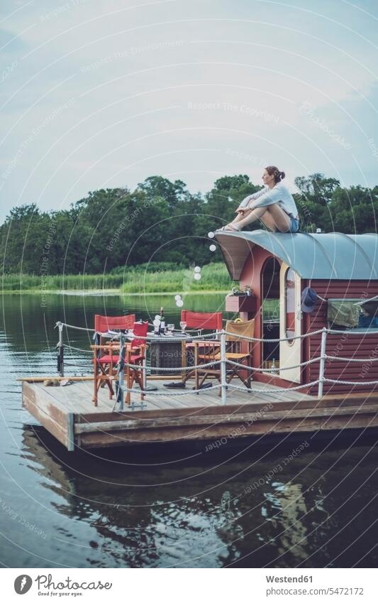 Mid adult woman sitting on roof of houseboat during sunset color image colour image outdoors location shots outdoor shot outdoor shots sunsets sundown