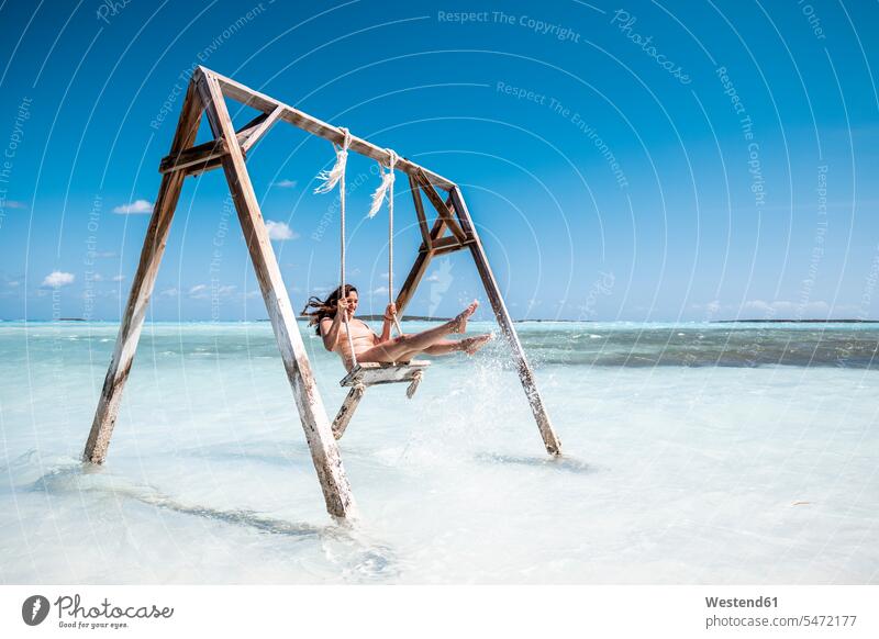Woman swinging on swing in the sea, Bahamas, Caribbean swim wear bathing costume bathing costumes bathing suit bathing suits Swimming Costume Swimming Suit