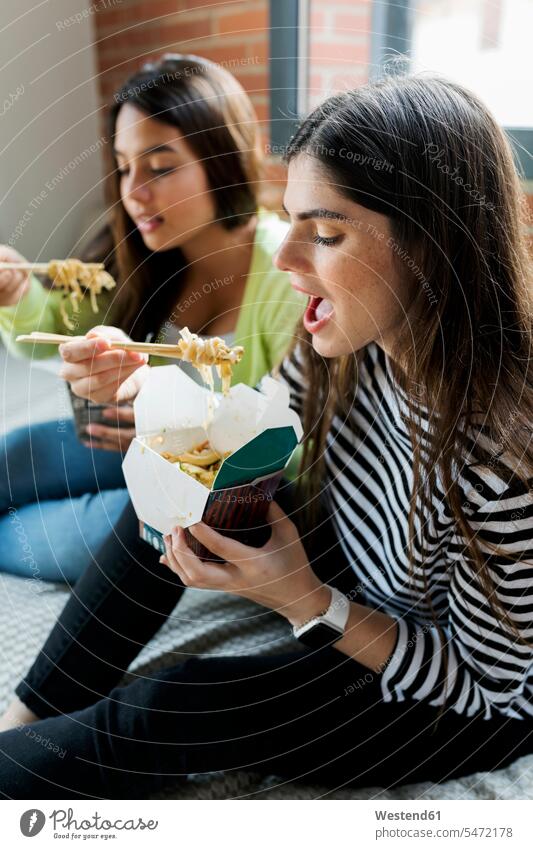 Two young women having Asian takeaway food at home eating Asiatic Asian Culture female friends woman females mate friendship Adults grown-ups grownups adult