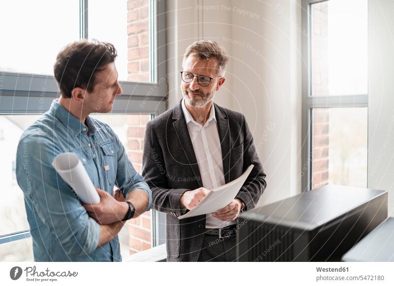 Two colleagues talking at the window in office speaking Businessman Business man Businessmen Business men windows offices office room office rooms