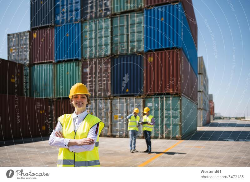Portrait of confident female worker in front of colleagues and cargo containers on industrial site port area harbour area harbor area port areas industry