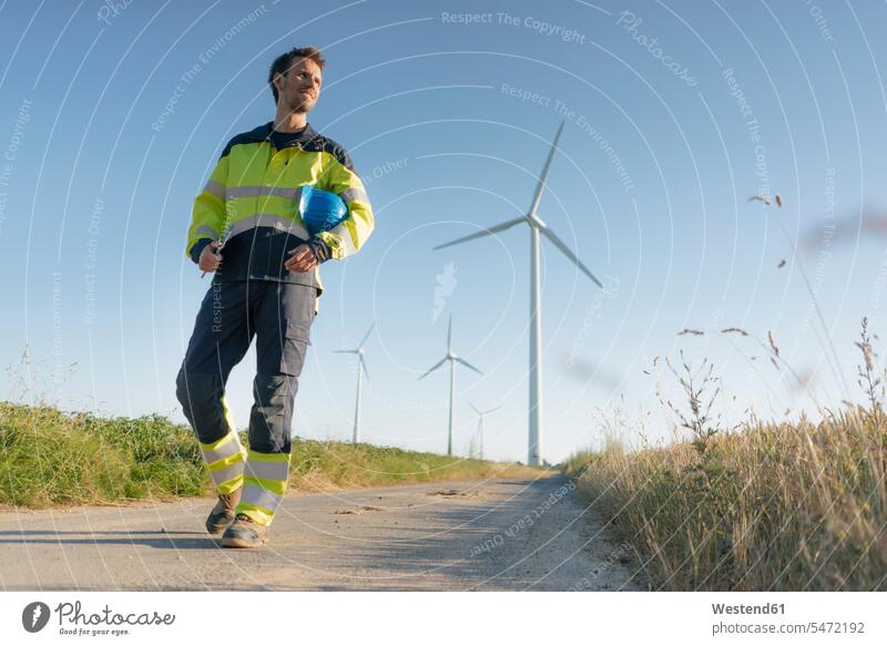 Engineer walking on field path at a wind farm country lane field road going wind park engineer engineers wind power plant wind turbine wind turbines wind energy