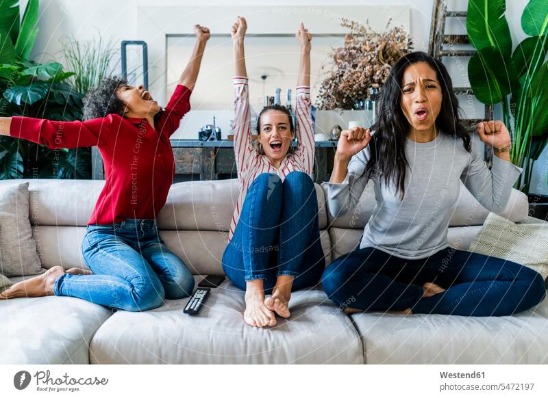 Three excited women on couch at home watching Tv and cheering woman females watching TV Looking At Tv watching television happiness happy excitement Exciting