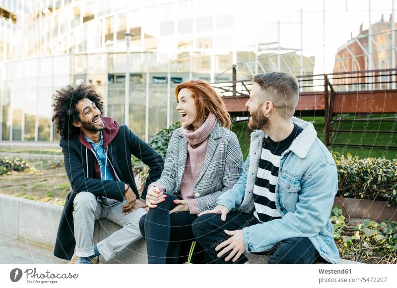 Three happy friends sitting in the city talking town cities towns happiness speaking Seated outdoors outdoor shots location shot location shots friendship