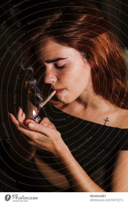 Young woman smoking marihuana at home tobacco Tobacco Products cigarettes cigarette lighters smoke flames flaming free time leisure time domestic room