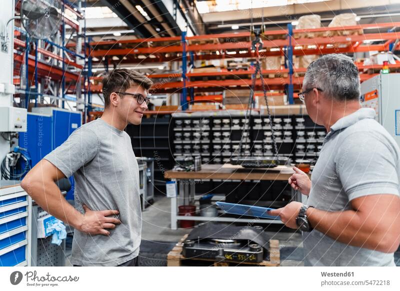 Smiling male coworker looking at mature engineer in illuminated factory color image colour image indoors indoor shot indoor shots interior interior view