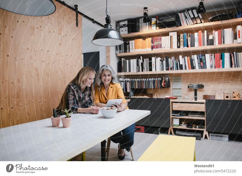 Smiling mother and adult daughter using tablet in loft office human human being human beings humans person persons caucasian appearance caucasian ethnicity
