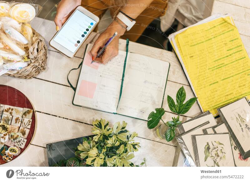 Top view of woman with smartphone taking notes in a small gardening shop Occupation Work job jobs profession professional occupation Tables pencil pencils pens